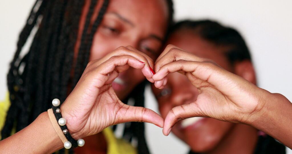 Mixed race mother and teen daughter making heart symbol with hands